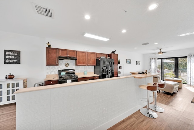 kitchen with black refrigerator with ice dispenser, wood-type flooring, french doors, a kitchen breakfast bar, and gas range