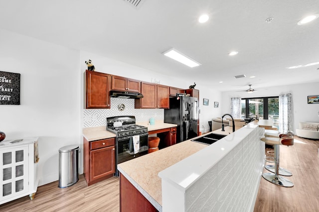 kitchen featuring black appliances, ceiling fan, sink, and a center island with sink