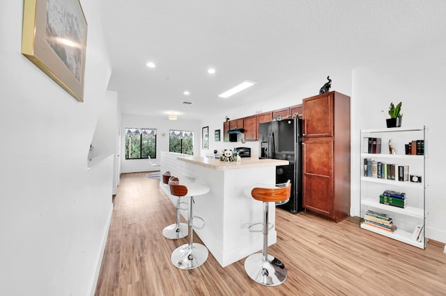 kitchen featuring a kitchen bar, light hardwood / wood-style floors, a kitchen island, and black fridge with ice dispenser