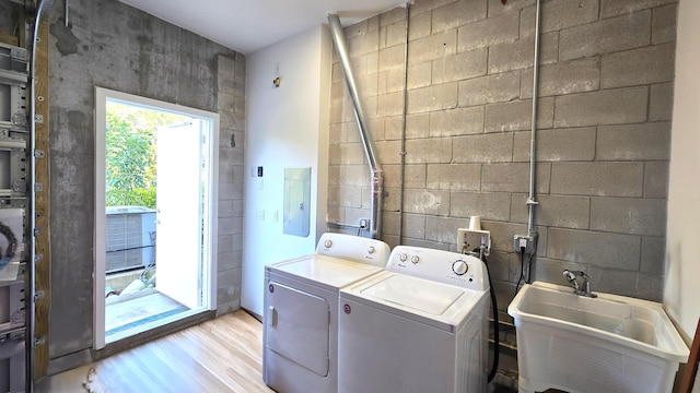 laundry room with light wood-type flooring, electric panel, washer and clothes dryer, and sink