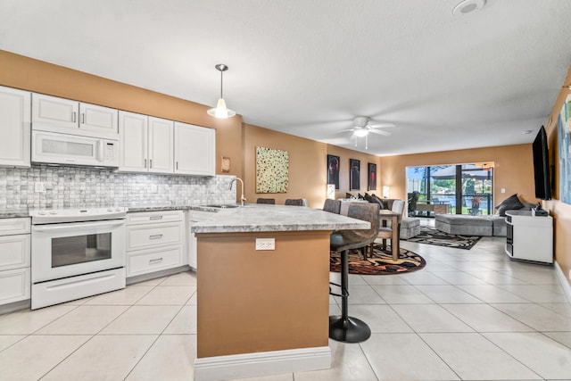 kitchen featuring pendant lighting, white appliances, white cabinets, sink, and a kitchen bar