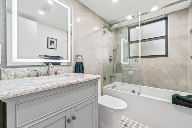 full bathroom with shower / bath combination with glass door, vanity, toilet, and tile walls