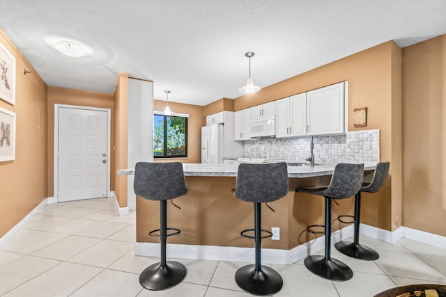 kitchen with hanging light fixtures, light tile patterned flooring, backsplash, white appliances, and white cabinets