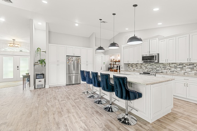 kitchen with an island with sink, lofted ceiling, decorative backsplash, white cabinets, and appliances with stainless steel finishes