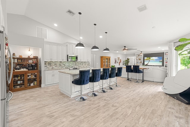 kitchen with ceiling fan, stainless steel appliances, lofted ceiling, a center island with sink, and white cabinets