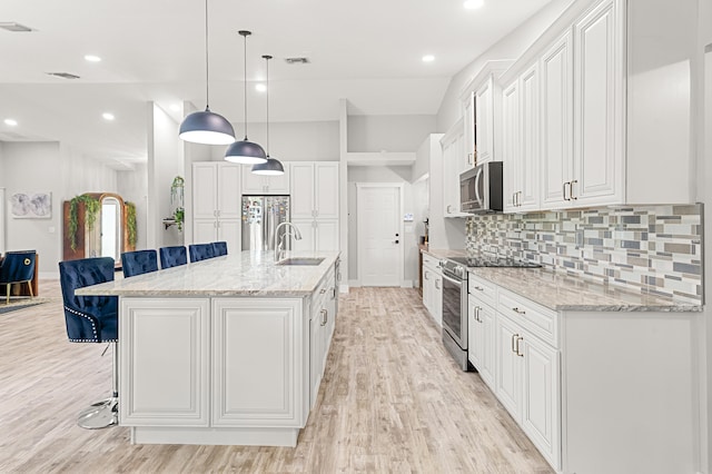 kitchen with a kitchen breakfast bar, stainless steel appliances, sink, white cabinetry, and an island with sink