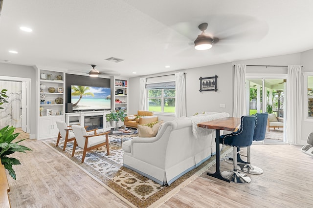 living room featuring light hardwood / wood-style flooring, built in features, and ceiling fan