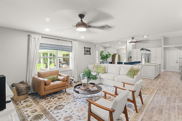 living room with a textured ceiling, light hardwood / wood-style floors, ceiling fan, and sink