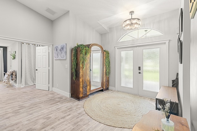 foyer featuring french doors, a towering ceiling, light hardwood / wood-style floors, and a notable chandelier