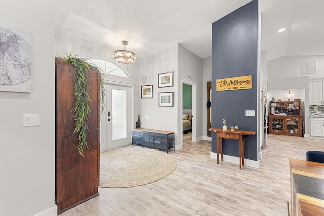 foyer entrance featuring an inviting chandelier, light hardwood / wood-style floors, and vaulted ceiling