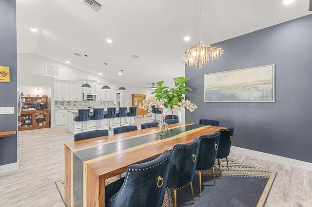 dining area with ceiling fan with notable chandelier, vaulted ceiling, and light wood-type flooring