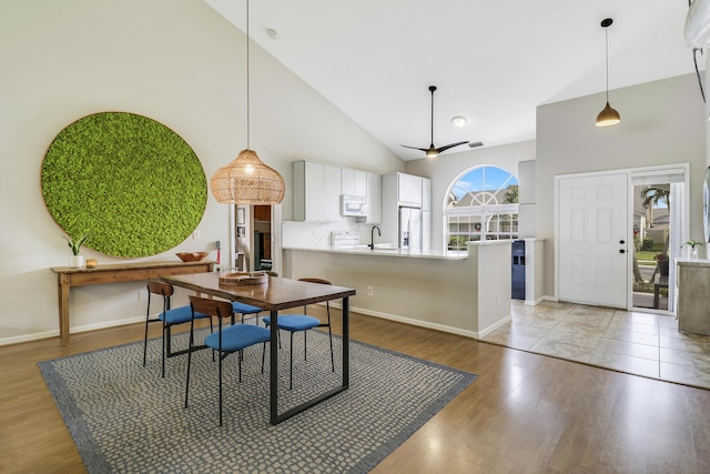 dining space with ceiling fan, light hardwood / wood-style flooring, high vaulted ceiling, and sink