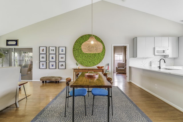 dining space with hardwood / wood-style floors, high vaulted ceiling, and sink