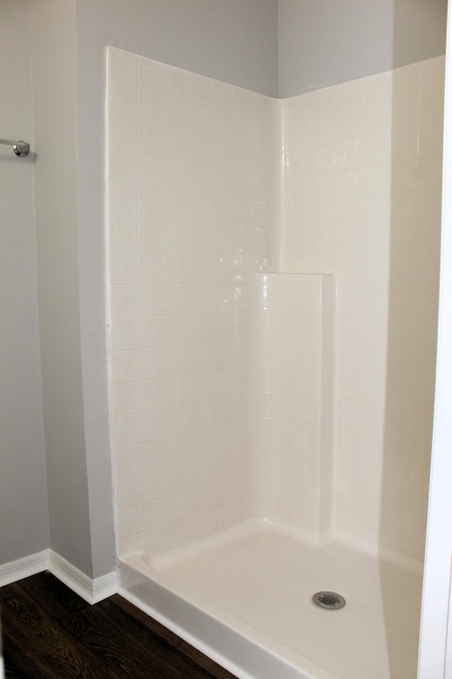 bathroom with tiled shower, wood finished floors, and baseboards