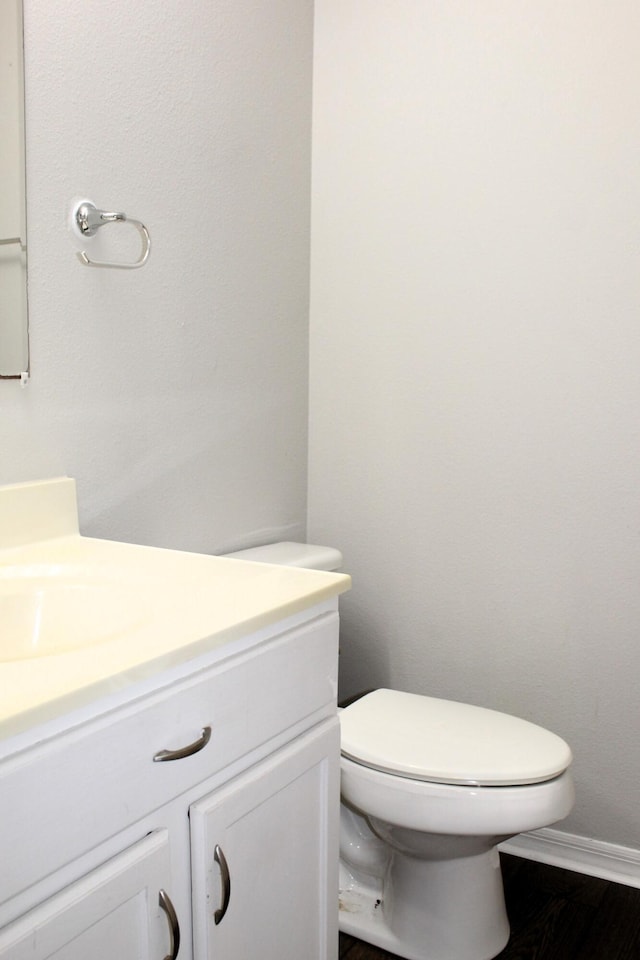 half bathroom with baseboards, vanity, and toilet