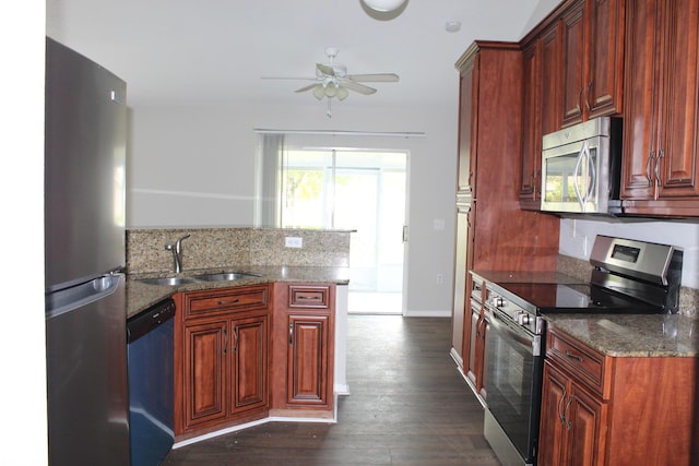 kitchen featuring stainless steel appliances, dark wood-type flooring, a sink, dark stone counters, and a peninsula