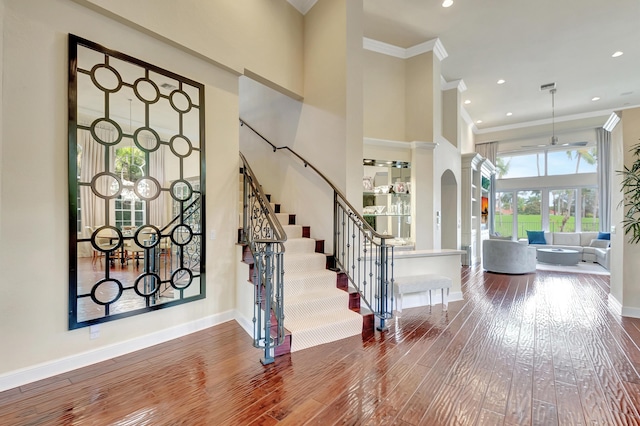 entryway with wood-type flooring, a towering ceiling, decorative columns, and ornamental molding