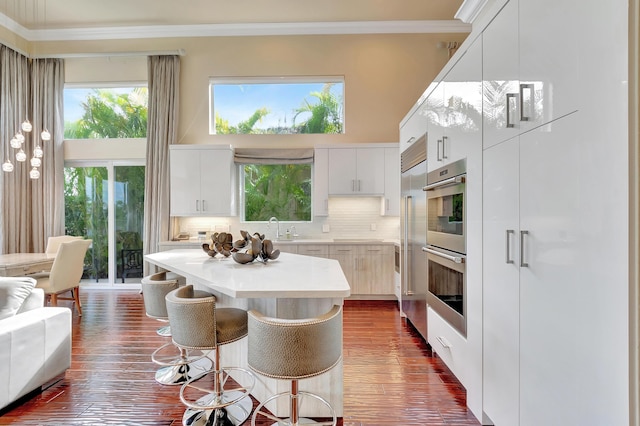 kitchen with a kitchen breakfast bar, tasteful backsplash, crown molding, sink, and white cabinets