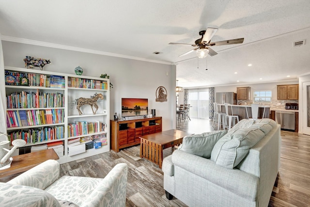 living room with a textured ceiling, light hardwood / wood-style flooring, ceiling fan, and crown molding