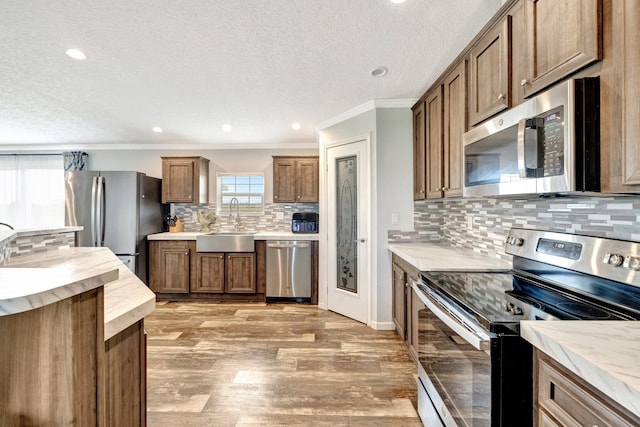 kitchen featuring crown molding, sink, decorative backsplash, light wood-type flooring, and appliances with stainless steel finishes