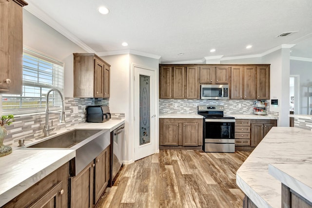 kitchen with appliances with stainless steel finishes, light wood-type flooring, tasteful backsplash, and sink