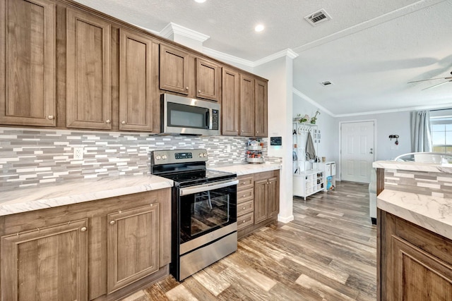 kitchen with backsplash, light hardwood / wood-style flooring, ornamental molding, a textured ceiling, and appliances with stainless steel finishes