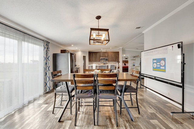 dining space with a textured ceiling, light hardwood / wood-style floors, an inviting chandelier, and crown molding