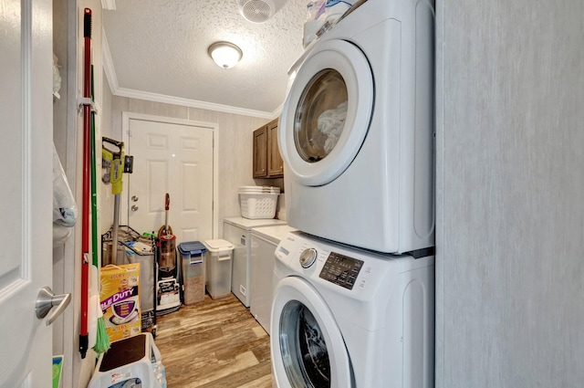 laundry room featuring cabinets, crown molding, stacked washing maching and dryer, a textured ceiling, and light wood-type flooring