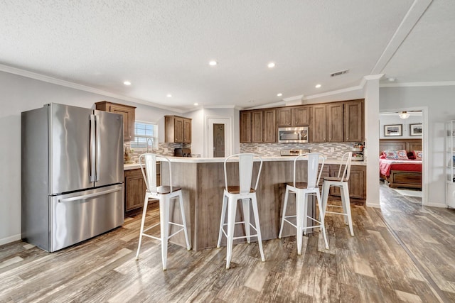 kitchen with a kitchen breakfast bar, crown molding, appliances with stainless steel finishes, tasteful backsplash, and a kitchen island