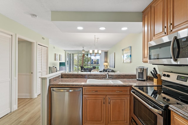 kitchen featuring sink, dark stone countertops, appliances with stainless steel finishes, light hardwood / wood-style floors, and a chandelier