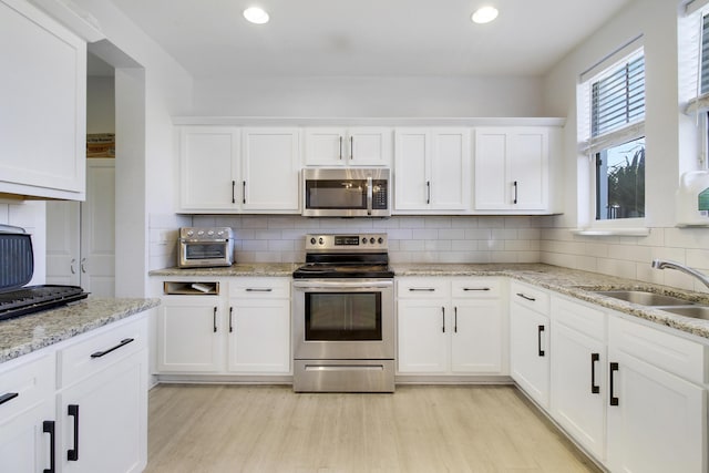 kitchen with appliances with stainless steel finishes, backsplash, sink, white cabinets, and light hardwood / wood-style floors