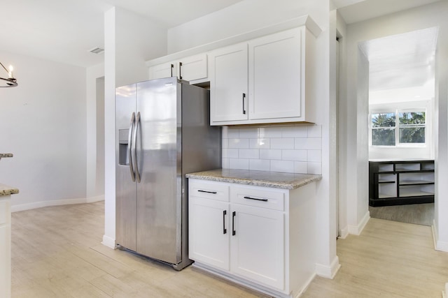 kitchen with white cabinets, stainless steel refrigerator with ice dispenser, light hardwood / wood-style flooring, tasteful backsplash, and light stone counters