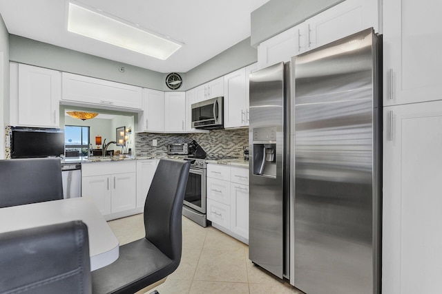 kitchen featuring stainless steel appliances, light tile patterned floors, sink, white cabinetry, and backsplash