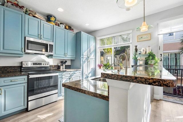 kitchen with blue cabinetry, sink, hanging light fixtures, stainless steel appliances, and light hardwood / wood-style floors