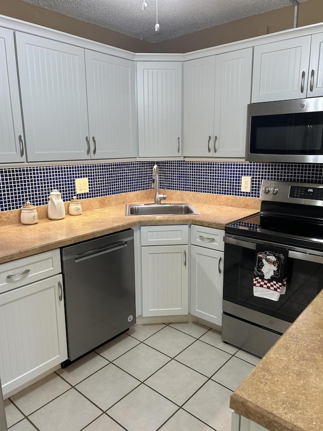 kitchen featuring light tile patterned flooring, sink, white cabinetry, stainless steel appliances, and decorative backsplash