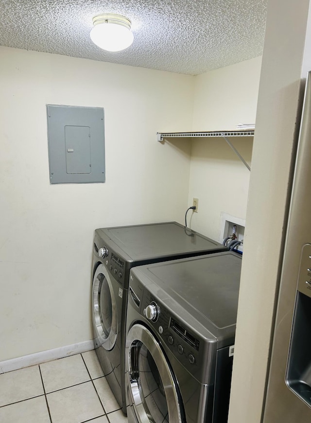 clothes washing area with washing machine and dryer, light tile patterned floors, electric panel, and a textured ceiling