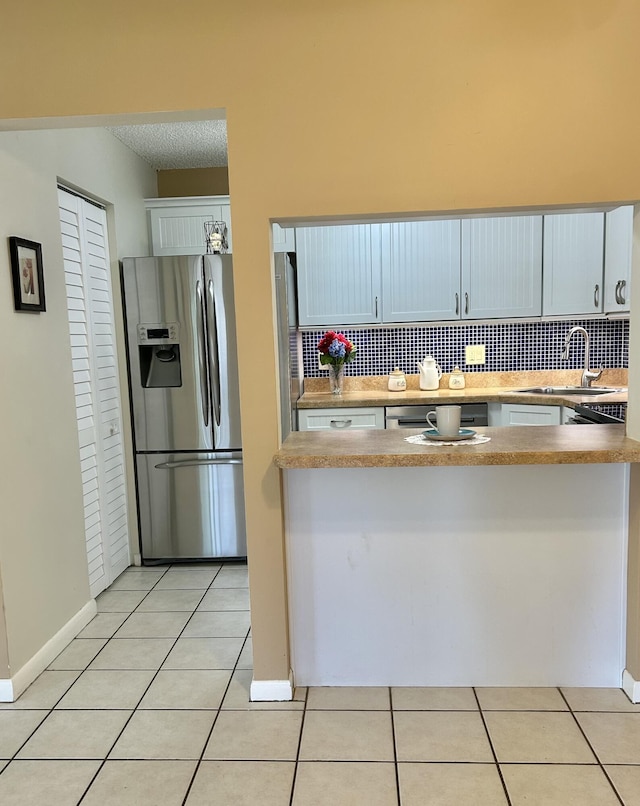 kitchen with stainless steel refrigerator with ice dispenser, sink, white cabinetry, light tile patterned floors, and backsplash