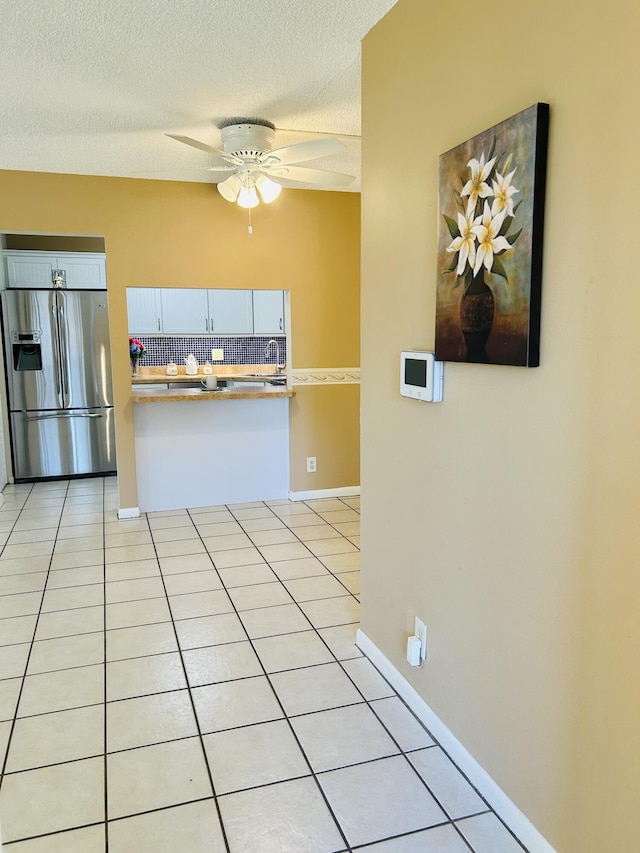 kitchen with baseboards, light tile patterned floors, stainless steel refrigerator with ice dispenser, a textured ceiling, and a ceiling fan