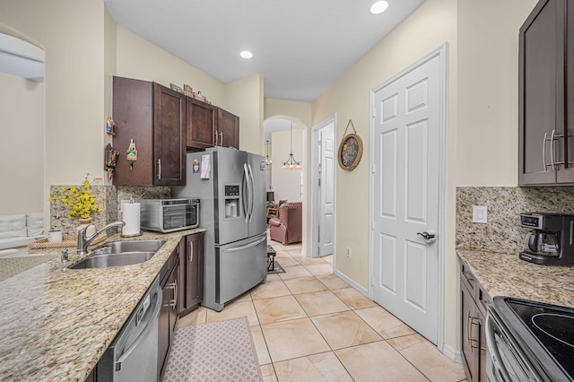 kitchen with backsplash, sink, light stone countertops, dark brown cabinetry, and stainless steel appliances