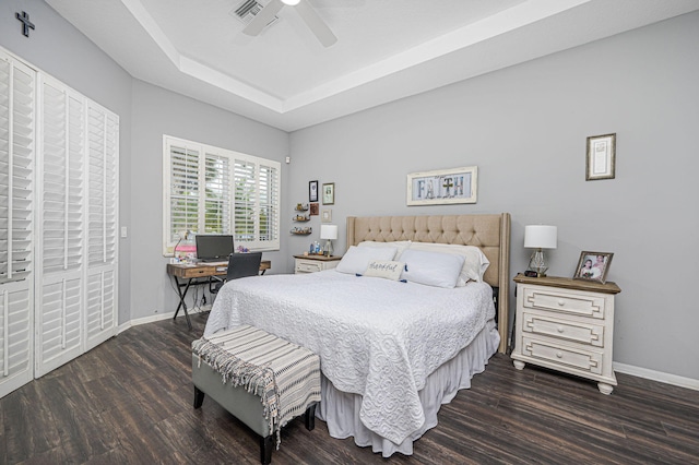 bedroom with ceiling fan, dark hardwood / wood-style floors, and a tray ceiling