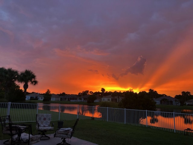 patio terrace at dusk featuring a lawn and a water view