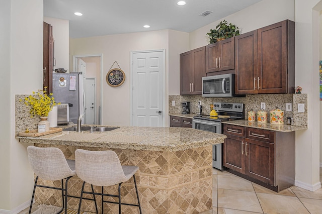 kitchen with decorative backsplash, kitchen peninsula, a breakfast bar, stainless steel appliances, and sink