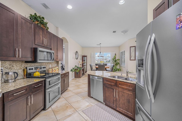 kitchen with backsplash, sink, hanging light fixtures, light stone counters, and stainless steel appliances