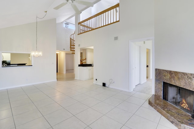 tiled living room with ceiling fan with notable chandelier, a towering ceiling, and a fireplace