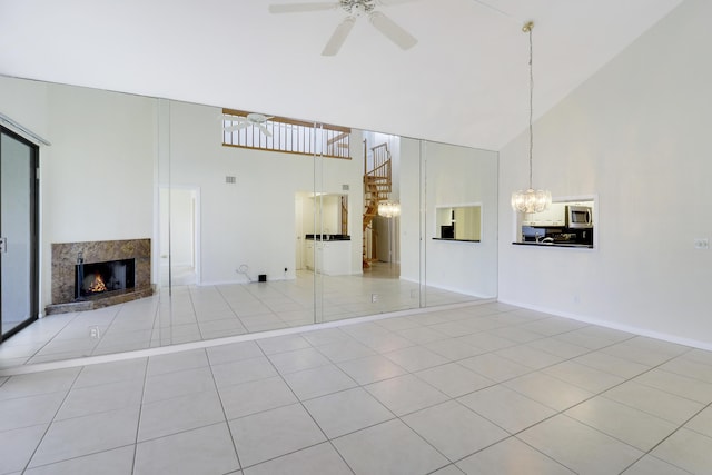 unfurnished living room with a premium fireplace, light tile patterned floors, high vaulted ceiling, and ceiling fan with notable chandelier