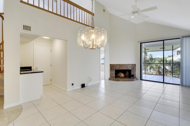 unfurnished living room featuring a premium fireplace, a towering ceiling, light tile patterned flooring, and ceiling fan with notable chandelier