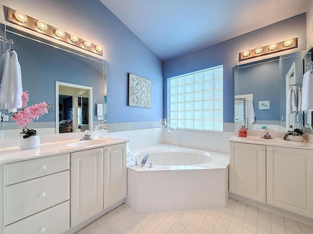 bathroom with vanity, vaulted ceiling, tiled bath, and tile patterned floors