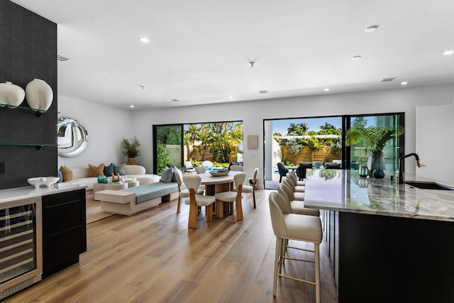 dining area featuring light wood-type flooring, wine cooler, and sink