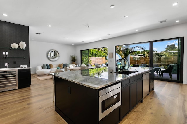 kitchen featuring wine cooler, a kitchen island with sink, sink, and light hardwood / wood-style flooring