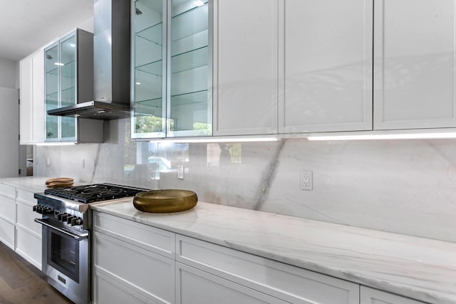 kitchen featuring white cabinetry, stainless steel range, light stone counters, and wall chimney range hood